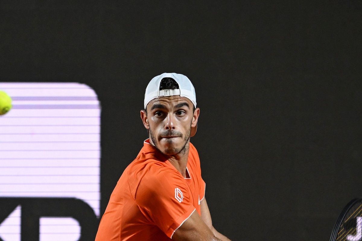 Francisco Cerúndolo playing a backhand in an orange shirt and white cap