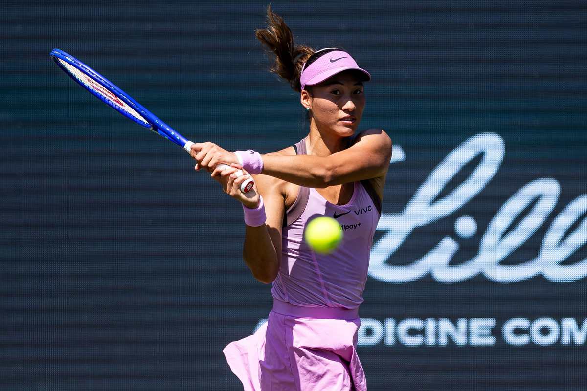 Zheng Qinwen playing a two-handed backhand in a pink and purple kit